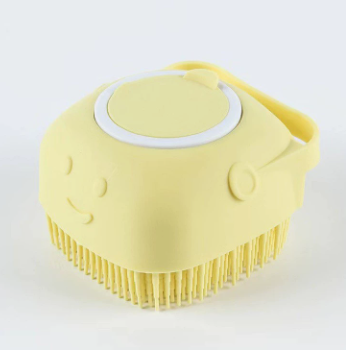 A pale yellow silicone facial cleansing brush with soft bristles, a smiley face design, and a carrying loop, shown on a white background.