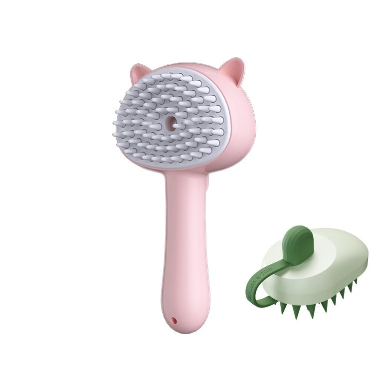 A pink pet grooming brush with cat-ear details and white silicone bristles, shown alongside a smaller green-and-white grooming attachment on a plain white background.
