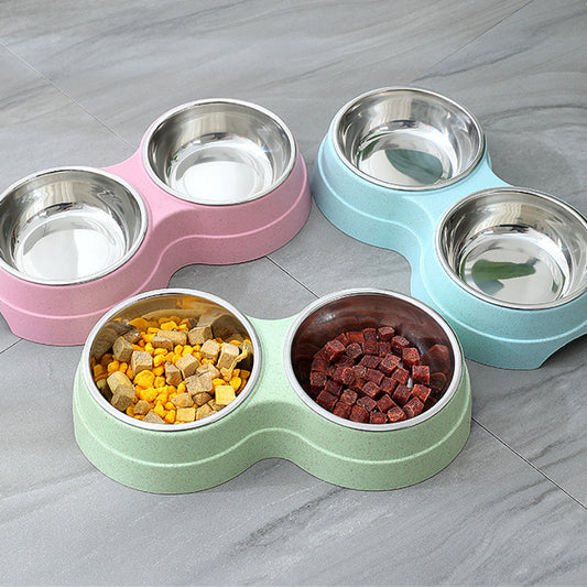 Set of pet bowls in pink, green, and blue with food inside on a gray surface.