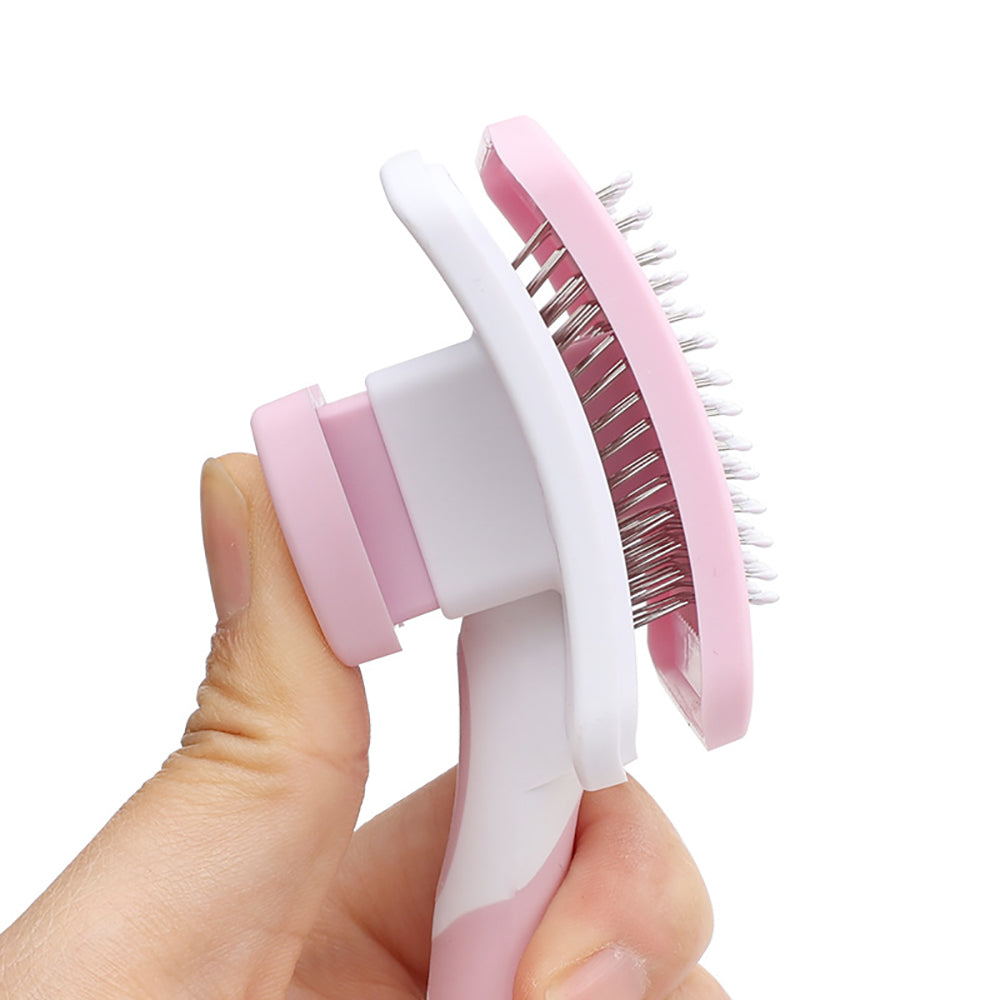 Pink and white grooming brush held in a hand against a white background