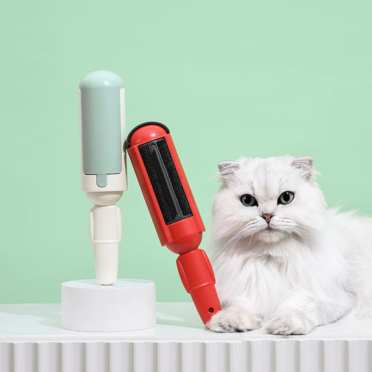 White cat sitting next to a red and white pet grooming brush on a light green background